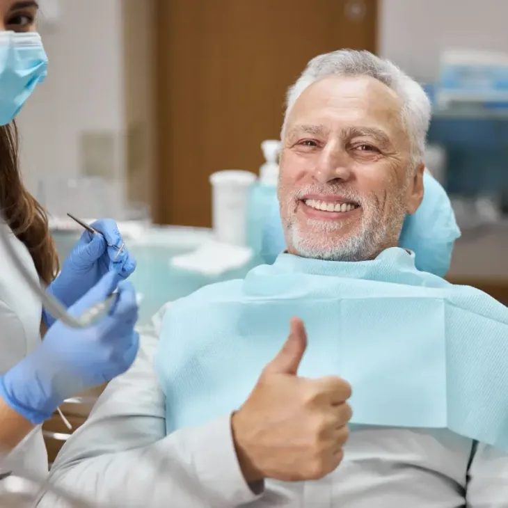 A smiling older man giving a thumbs up from the dental chair