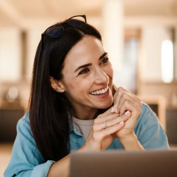 A smiling woman resting her chin on her hands at a desk