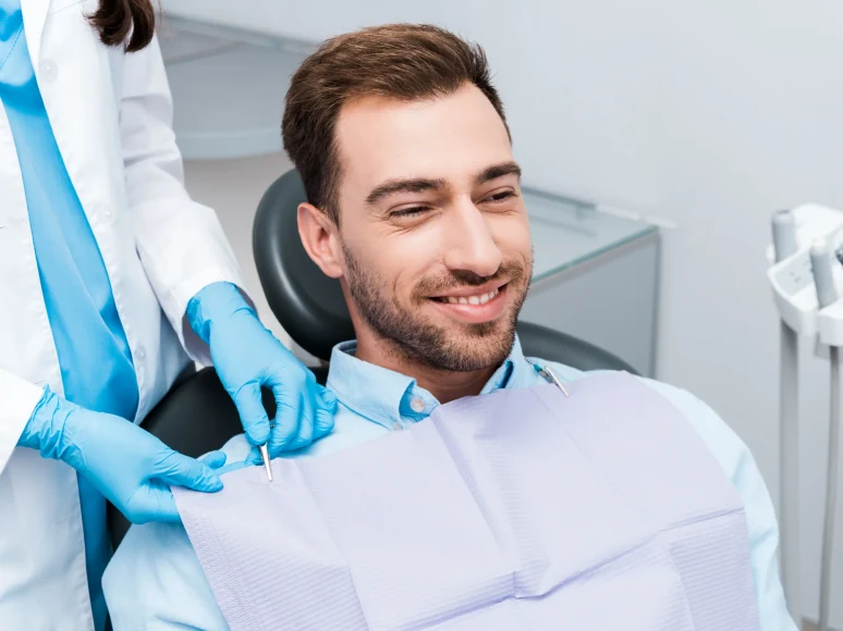 A dental assistant attends to a smiling male patient during a routine checkup