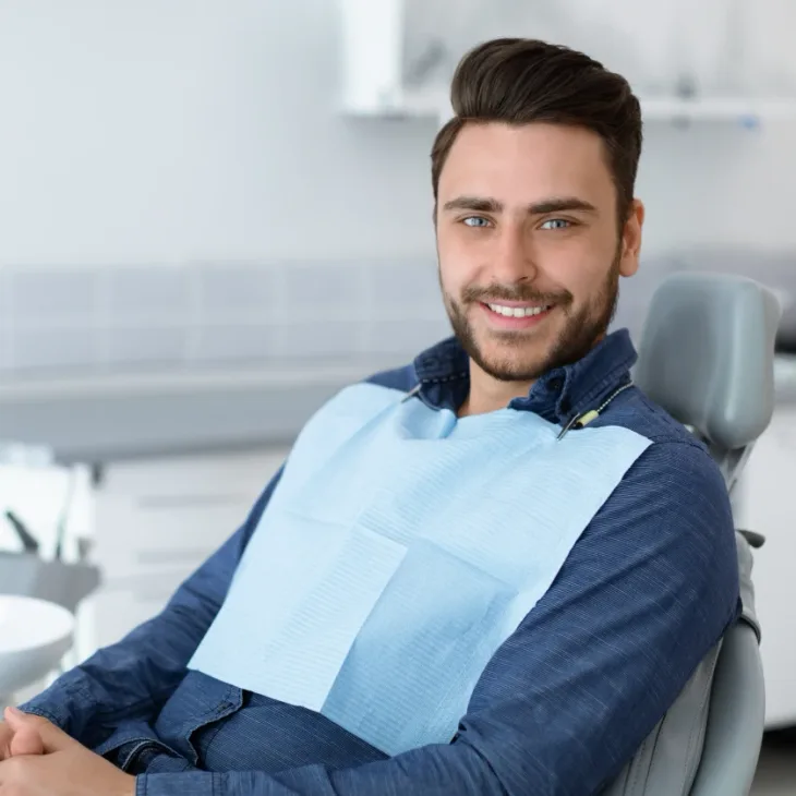 A patient sitting back comfortably in the dental chair, wearing a bib