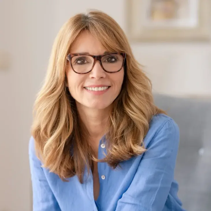 A smiling woman in glasses seated indoors