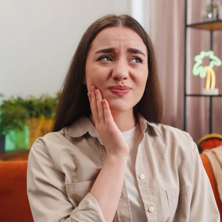 A woman holding her cheek, wincing with toothache