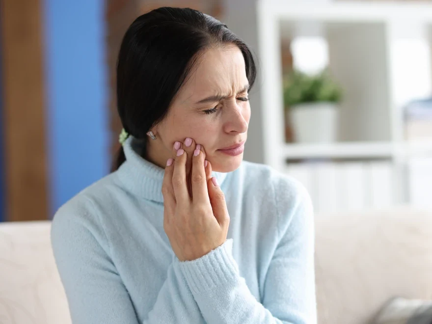 A patient wincing and holding her cheek from tooth sensitivity