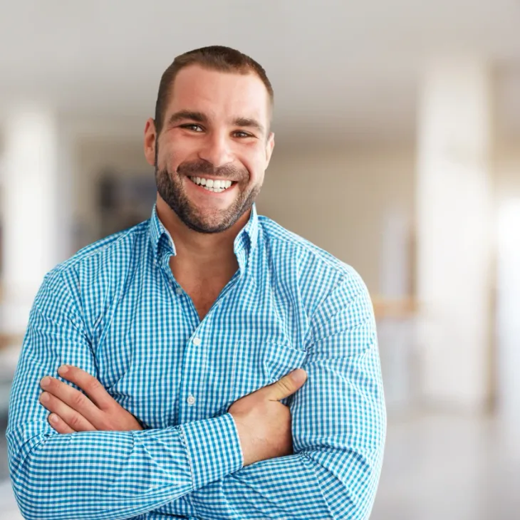 A smiling man with his arms folded indoors