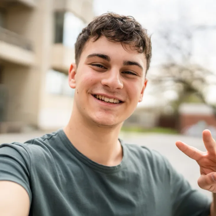A smiling young man making a peace sign outdoors