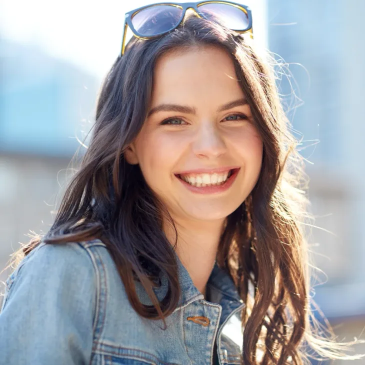 A smiling young woman outdoors with sunglasses on her head