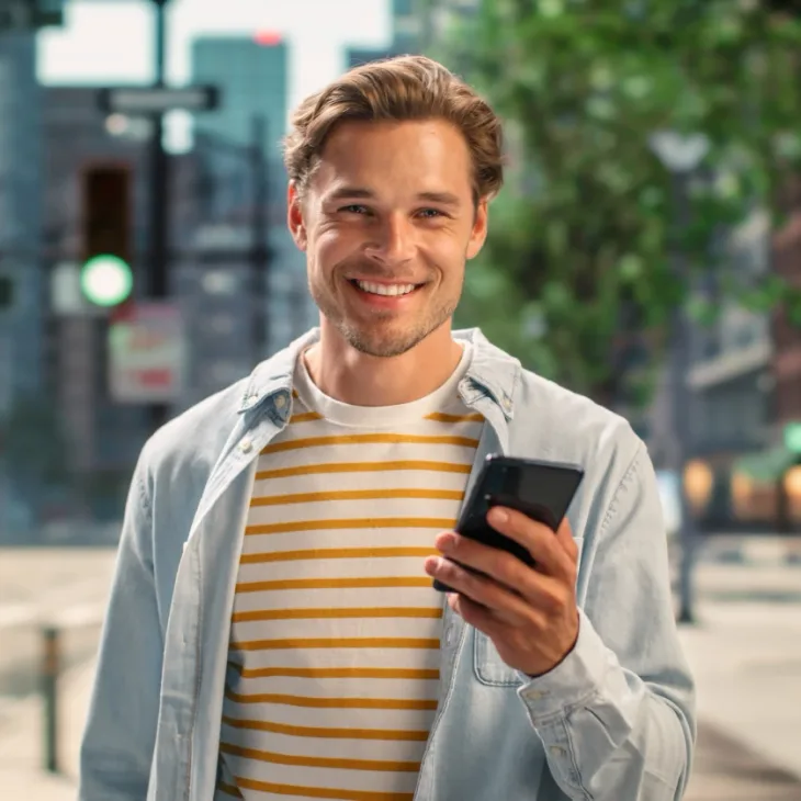 A smiling man on a city street holding his phone