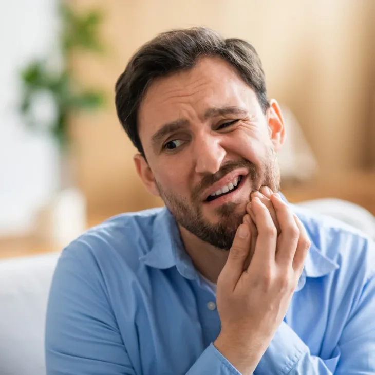 A man wincing and holding his jaw