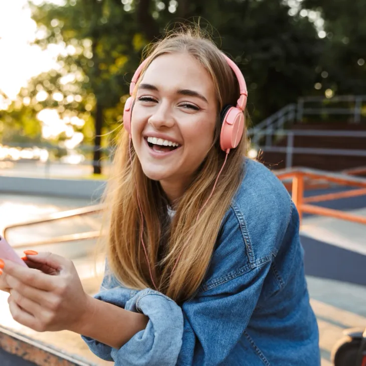 A smiling young woman outdoors wearing headphones