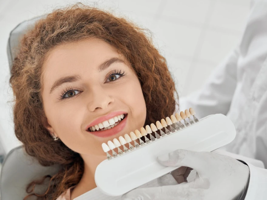 A dental shade guide held up beside a smiling patient to match her tooth color