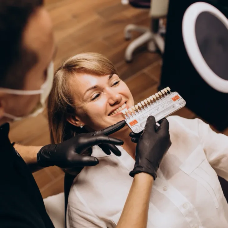 A dental shade guide held beside a patient's smile in the chair