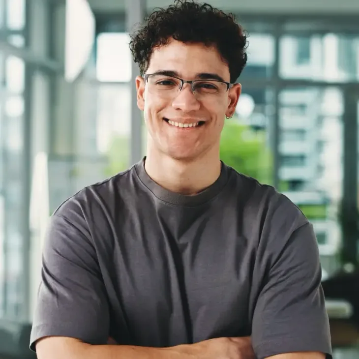A smiling young man in glasses with his arms folded