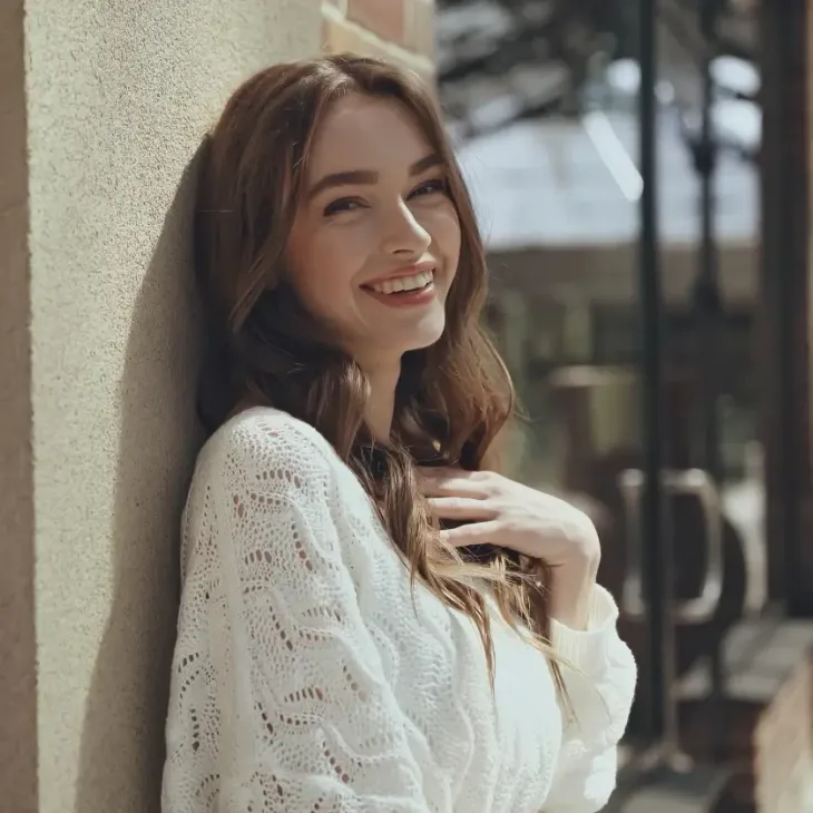 A smiling young woman leaning against a wall