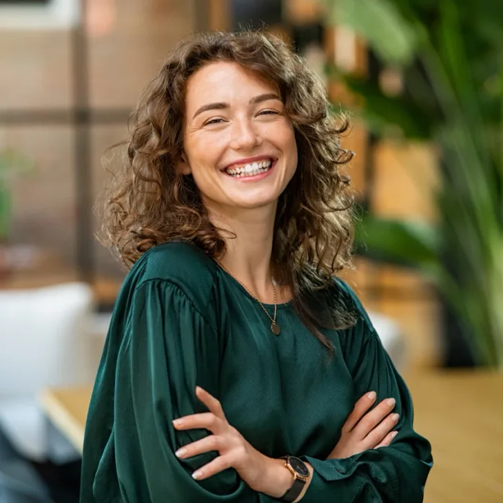 A laughing woman with curly hair in a green blouse