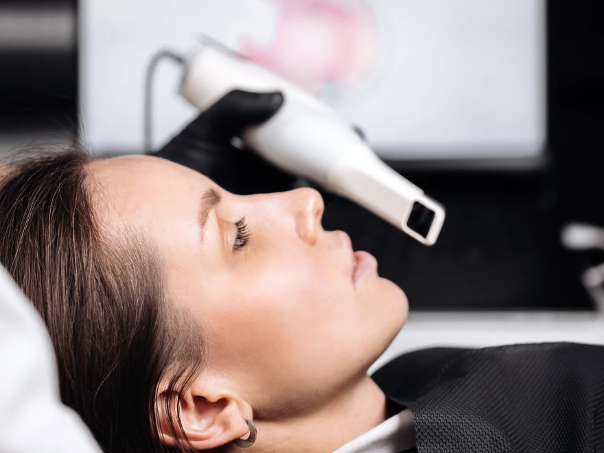 A patient reclining while a handheld scanner builds a 3D model on the screen behind