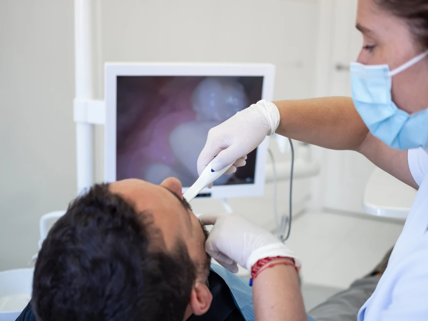 A hygienist guiding an intraoral camera while the live view shows on screen